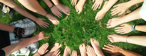 Billede af en gruppe unge menneskers hænder og fødder i en rundkreds på en græsplæne